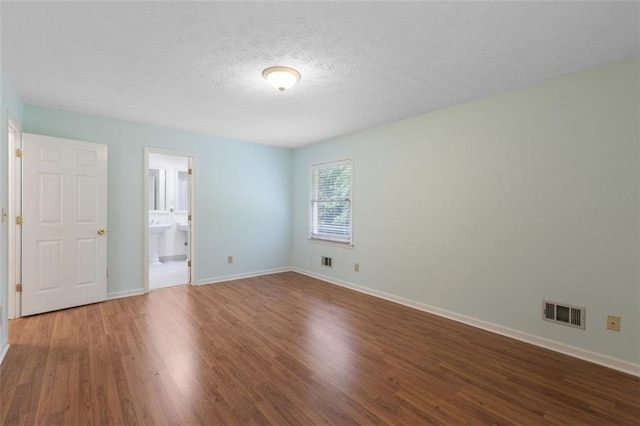 unfurnished bedroom with hardwood / wood-style floors, a textured ceiling, and ensuite bath