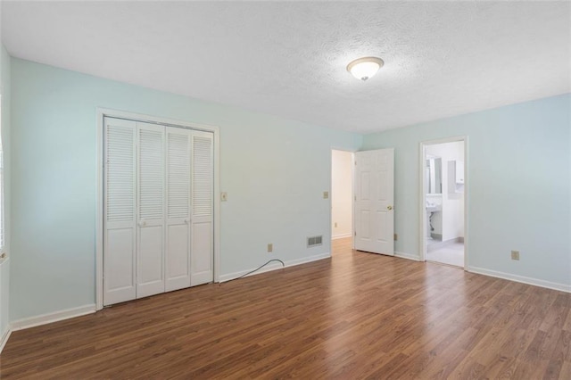 unfurnished bedroom featuring ensuite bath, a closet, a textured ceiling, and hardwood / wood-style flooring