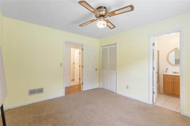 unfurnished bedroom with ensuite bathroom, ceiling fan, light carpet, and a closet