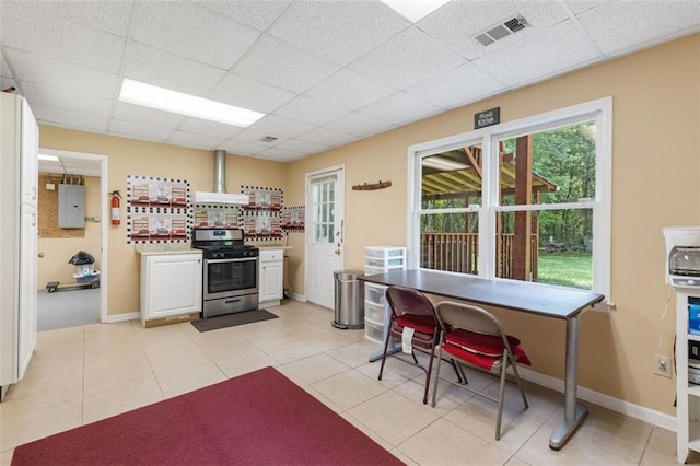 kitchen featuring wall chimney exhaust hood, stainless steel stove, electric panel, a paneled ceiling, and white cabinets