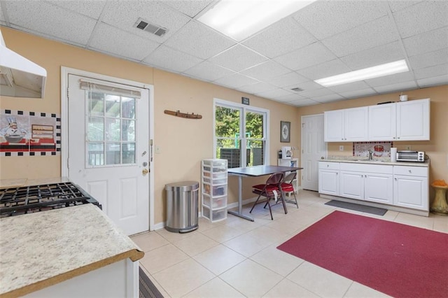 kitchen featuring white cabinets, a paneled ceiling, and range hood