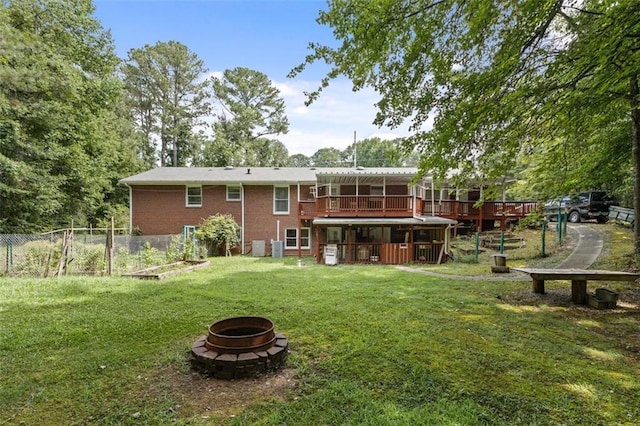 rear view of house with a deck, a lawn, and a fire pit