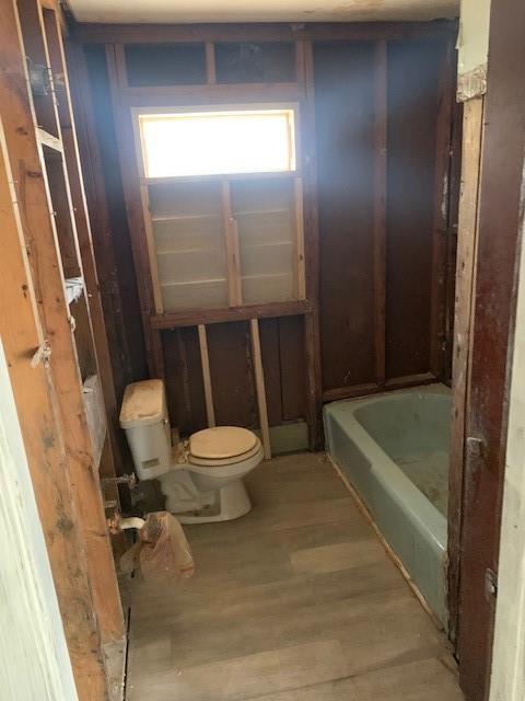 full bathroom with toilet, a tub to relax in, and wood finished floors