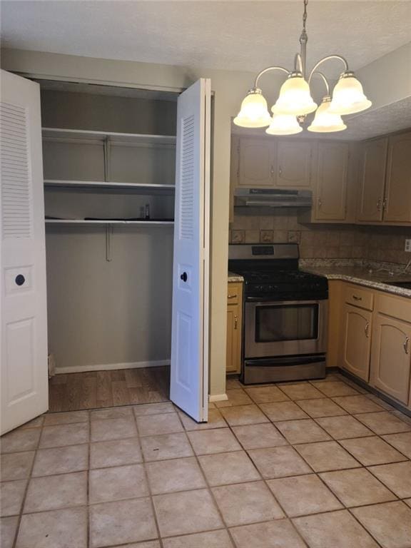 kitchen with light tile patterned floors, an inviting chandelier, hanging light fixtures, backsplash, and stainless steel range with gas stovetop