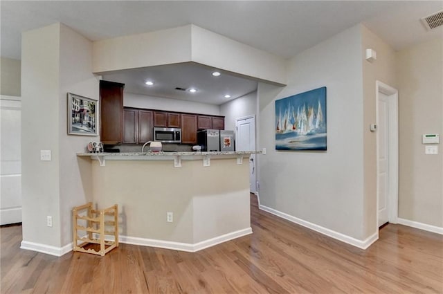 4165 Hammond Bridge Dr, Suwanee, GA 30024 - kitchen with stainless steel microwave, freestanding refrigerator, light wood finished floors, a kitchen breakfast bar, and a peninsula