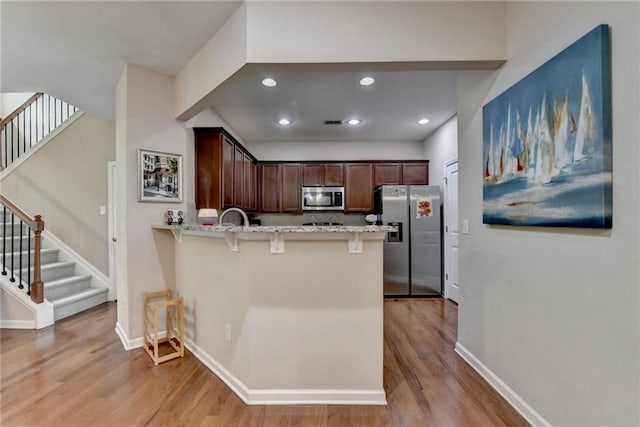 4165 Hammond Bridge Dr, Suwanee, GA 30024 - kitchen featuring appliances with stainless steel finishes, light stone countertops, light wood-style flooring, a breakfast bar, and a peninsula
