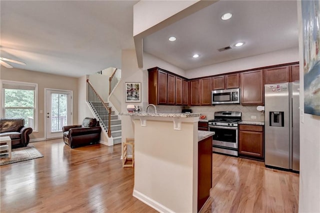4165 Hammond Bridge Dr, Suwanee, GA 30024 - kitchen featuring appliances with stainless steel finishes, open floor plan, a breakfast bar area, a peninsula, and light wood-type flooring