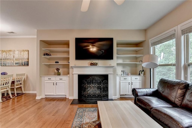4165 Hammond Bridge Dr, Suwanee, GA 30024 - living room featuring light wood-style flooring, a ceiling fan, built in shelves, a fireplace with flush hearth, and crown molding