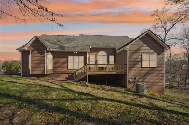 back house at dusk with central AC unit, a yard, and a deck