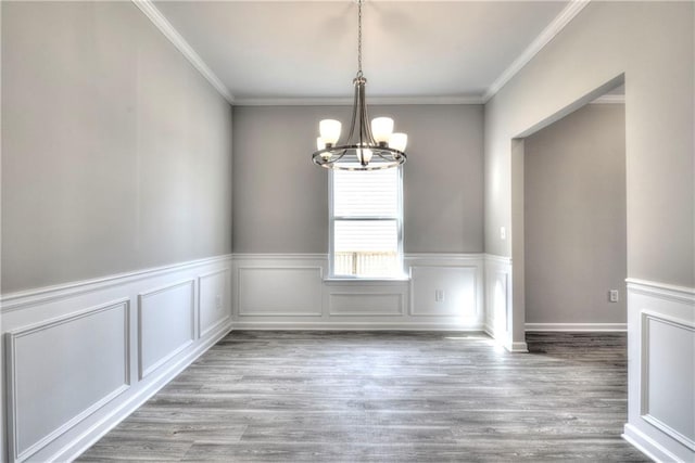 unfurnished dining area featuring light wood-type flooring, crown molding, and a notable chandelier