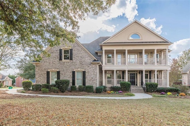 greek revival inspired property with a balcony, covered porch, and a front lawn