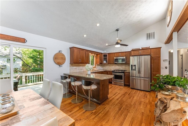 kitchen with stainless steel appliances, a peninsula, visible vents, light wood-style floors, and lofted ceiling