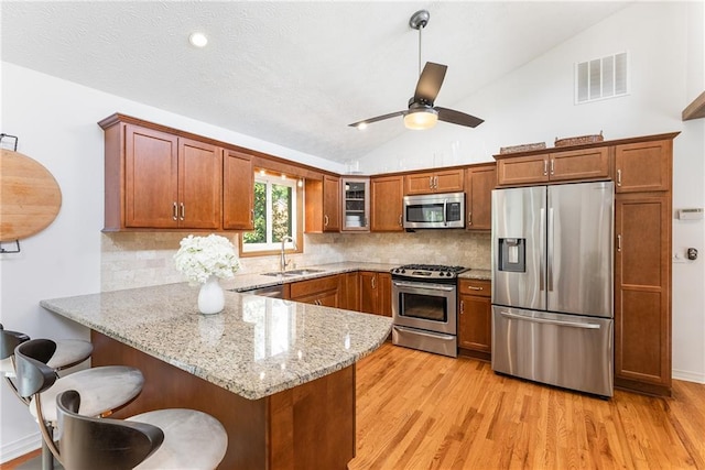 kitchen featuring visible vents, a sink, a peninsula, brown cabinetry, and appliances with stainless steel finishes
