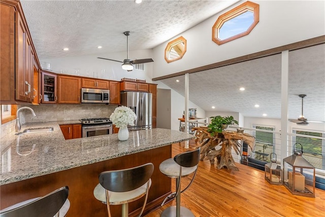 kitchen featuring a textured ceiling, a sink, ceiling fan, stainless steel appliances, and light wood finished floors