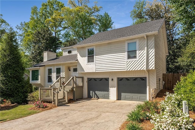 split level home featuring driveway, a chimney, fence, an attached garage, and a shingled roof