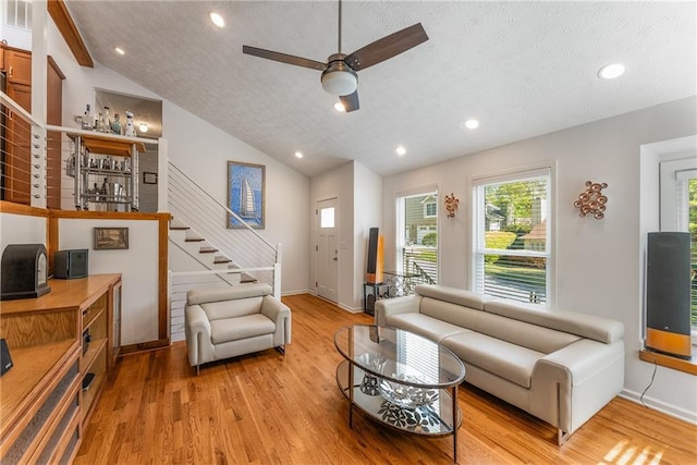 living room with light wood finished floors, vaulted ceiling, a textured ceiling, and a healthy amount of sunlight