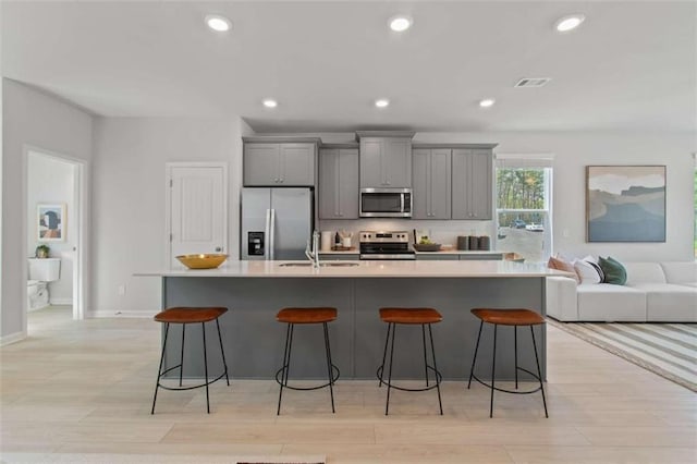 kitchen with sink, gray cabinetry, stainless steel appliances, light hardwood / wood-style flooring, and a spacious island