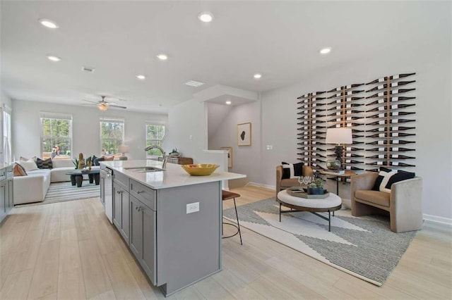 kitchen with gray cabinetry, light hardwood / wood-style floors, a kitchen bar, a center island with sink, and sink