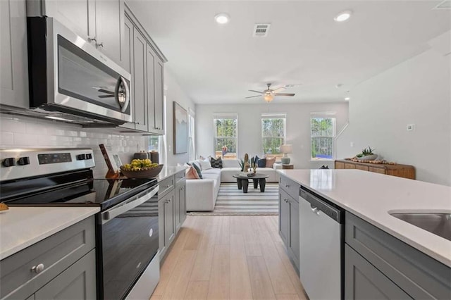 kitchen with ceiling fan, tasteful backsplash, light hardwood / wood-style flooring, gray cabinets, and stainless steel appliances