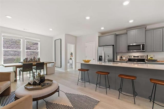 kitchen featuring gray cabinetry, light wood-type flooring, appliances with stainless steel finishes, and a kitchen bar