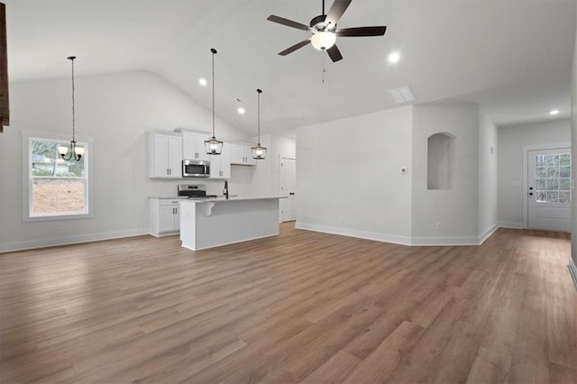 unfurnished living room featuring ceiling fan with notable chandelier, light wood-style floors, baseboards, and high vaulted ceiling