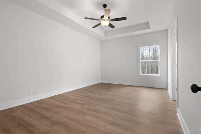 unfurnished room featuring baseboards, a raised ceiling, wood finished floors, and a ceiling fan