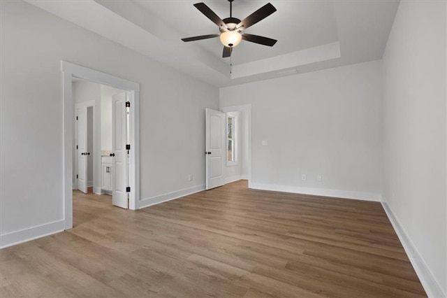 unfurnished bedroom featuring a ceiling fan, a raised ceiling, baseboards, and wood finished floors