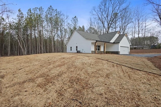 view of side of property featuring central air condition unit, an attached garage, driveway, and stone siding