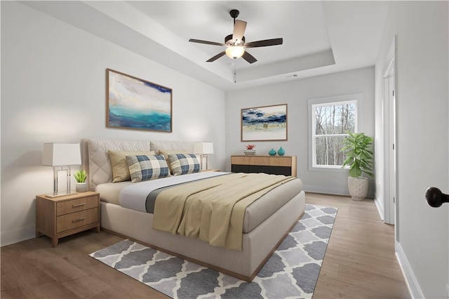 bedroom with light wood-style flooring, baseboards, a tray ceiling, and ceiling fan