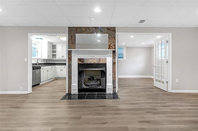 unfurnished living room with a large fireplace, a paneled ceiling, plenty of natural light, and light hardwood / wood-style floors