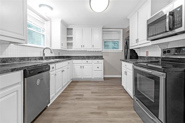 kitchen with appliances with stainless steel finishes, white cabinetry, light hardwood / wood-style floors, and backsplash