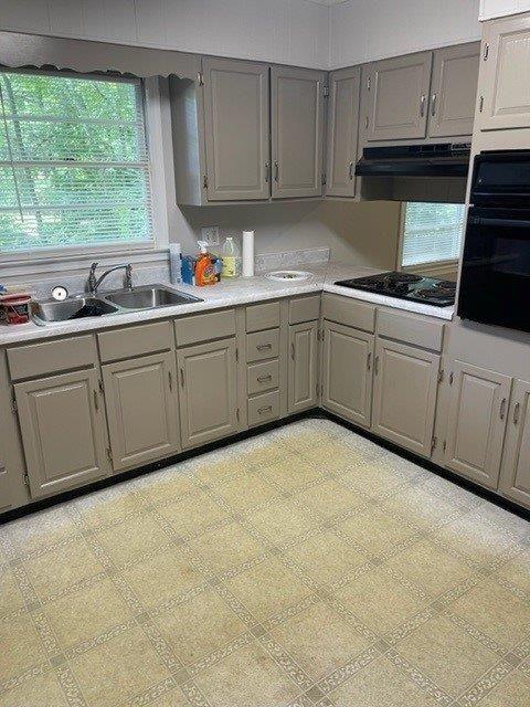 kitchen featuring light floors, under cabinet range hood, light countertops, gray cabinetry, and black appliances