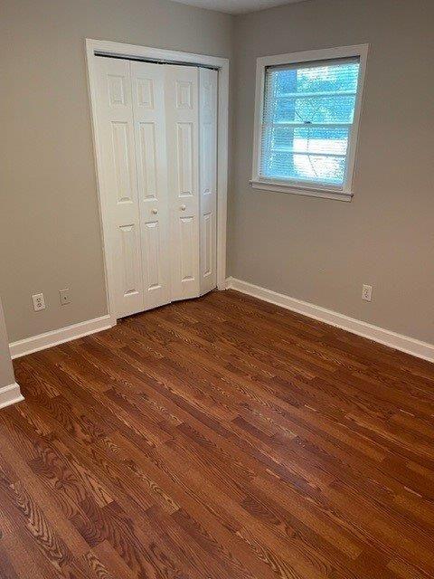 unfurnished bedroom with dark wood-style flooring, a closet, and baseboards