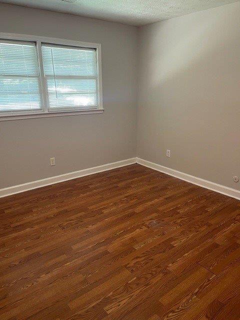 spare room with dark wood-style floors, a textured ceiling, and baseboards