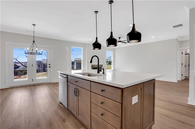 kitchen featuring a sink, visible vents, light countertops, stainless steel dishwasher, and a center island with sink