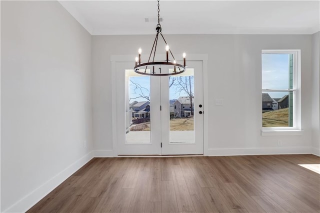 unfurnished dining area with baseboards, ornamental molding, wood finished floors, and an inviting chandelier