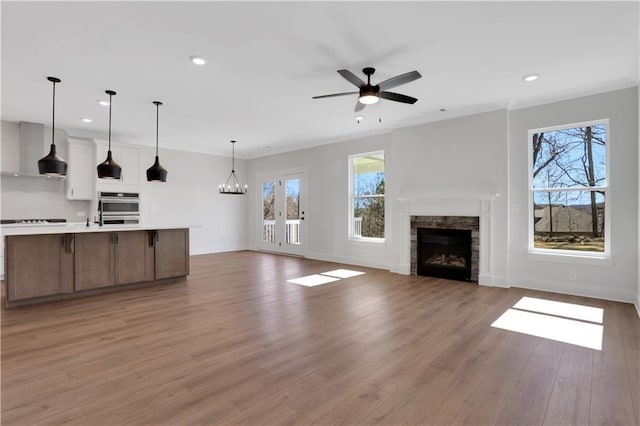 unfurnished living room featuring recessed lighting, a stone fireplace, wood finished floors, baseboards, and ceiling fan with notable chandelier