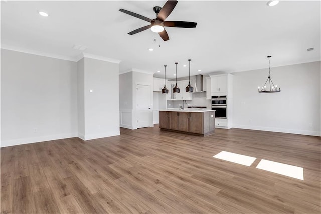 unfurnished living room featuring ceiling fan with notable chandelier, a sink, baseboards, light wood finished floors, and crown molding