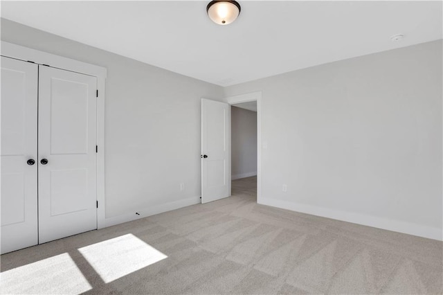 unfurnished bedroom featuring baseboards, a closet, and light colored carpet