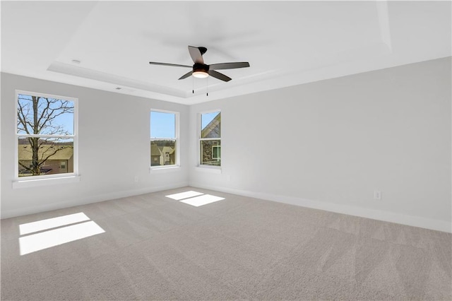 empty room with a tray ceiling, light colored carpet, and baseboards