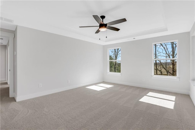 unfurnished room featuring a raised ceiling, light colored carpet, ceiling fan, and baseboards