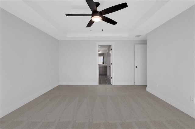 empty room featuring ceiling fan, a raised ceiling, light colored carpet, and baseboards