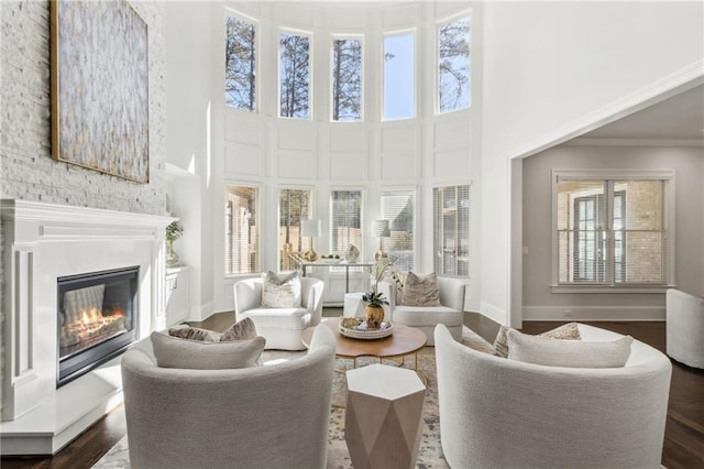 living room featuring baseboards, dark wood finished floors, a glass covered fireplace, crown molding, and a high ceiling