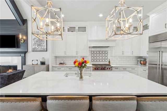 kitchen featuring stainless steel appliances, tasteful backsplash, white cabinets, a lit fireplace, and a notable chandelier