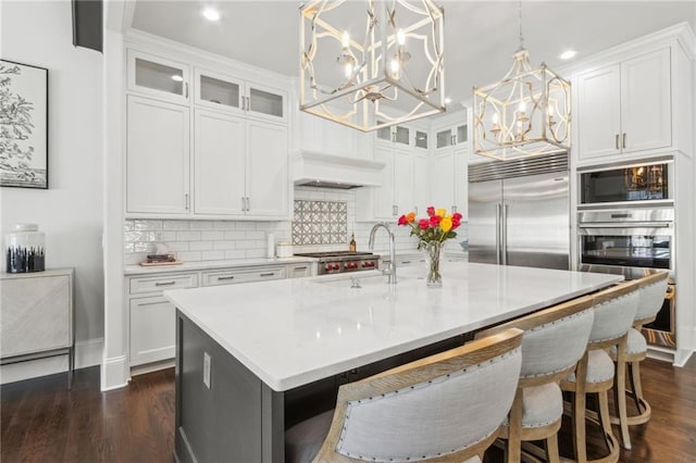 kitchen featuring a sink, a notable chandelier, built in appliances, light countertops, and tasteful backsplash