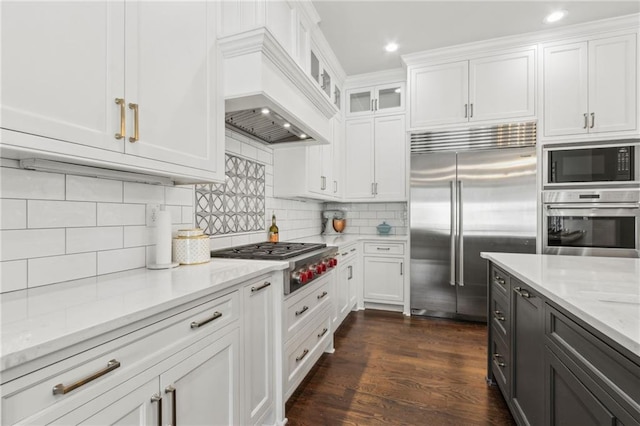kitchen featuring built in appliances, backsplash, light stone countertops, and white cabinetry