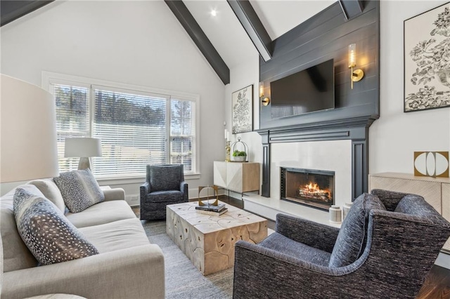living area with beam ceiling, a warm lit fireplace, wood finished floors, and high vaulted ceiling