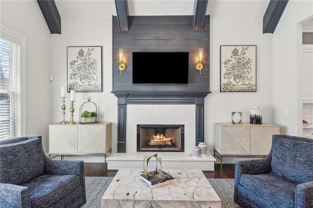 living area featuring a lit fireplace, beam ceiling, and wood finished floors