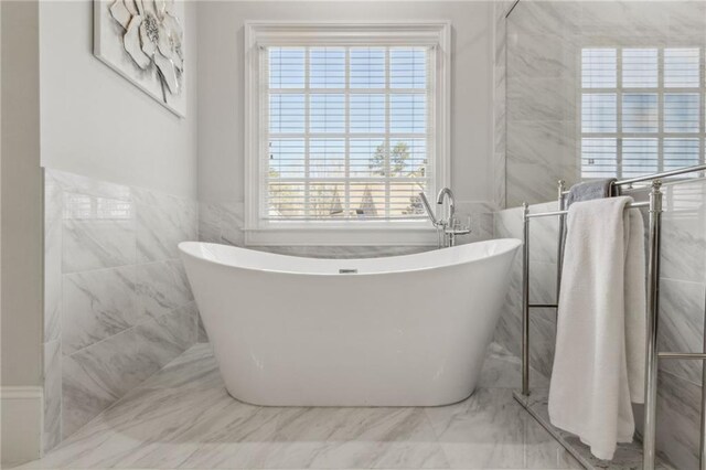 full bath featuring wainscoting, a soaking tub, tile walls, and marble finish floor