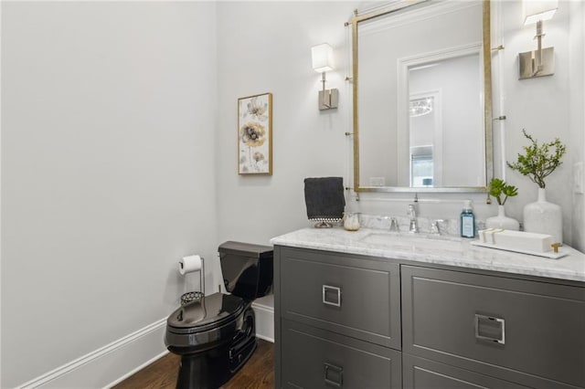 half bath featuring vanity, toilet, baseboards, and wood finished floors